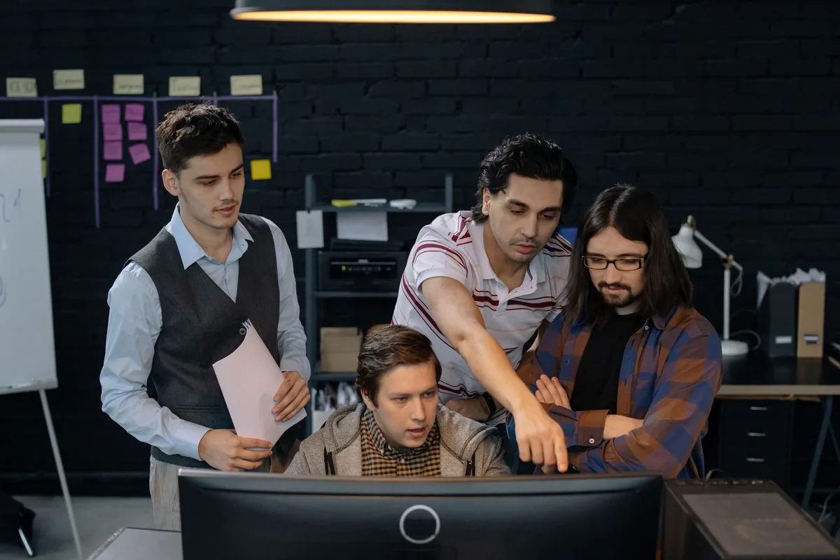 Equipo de desarrollo trabajando en conjunto frente a un computador, revisando código de un proyecto
